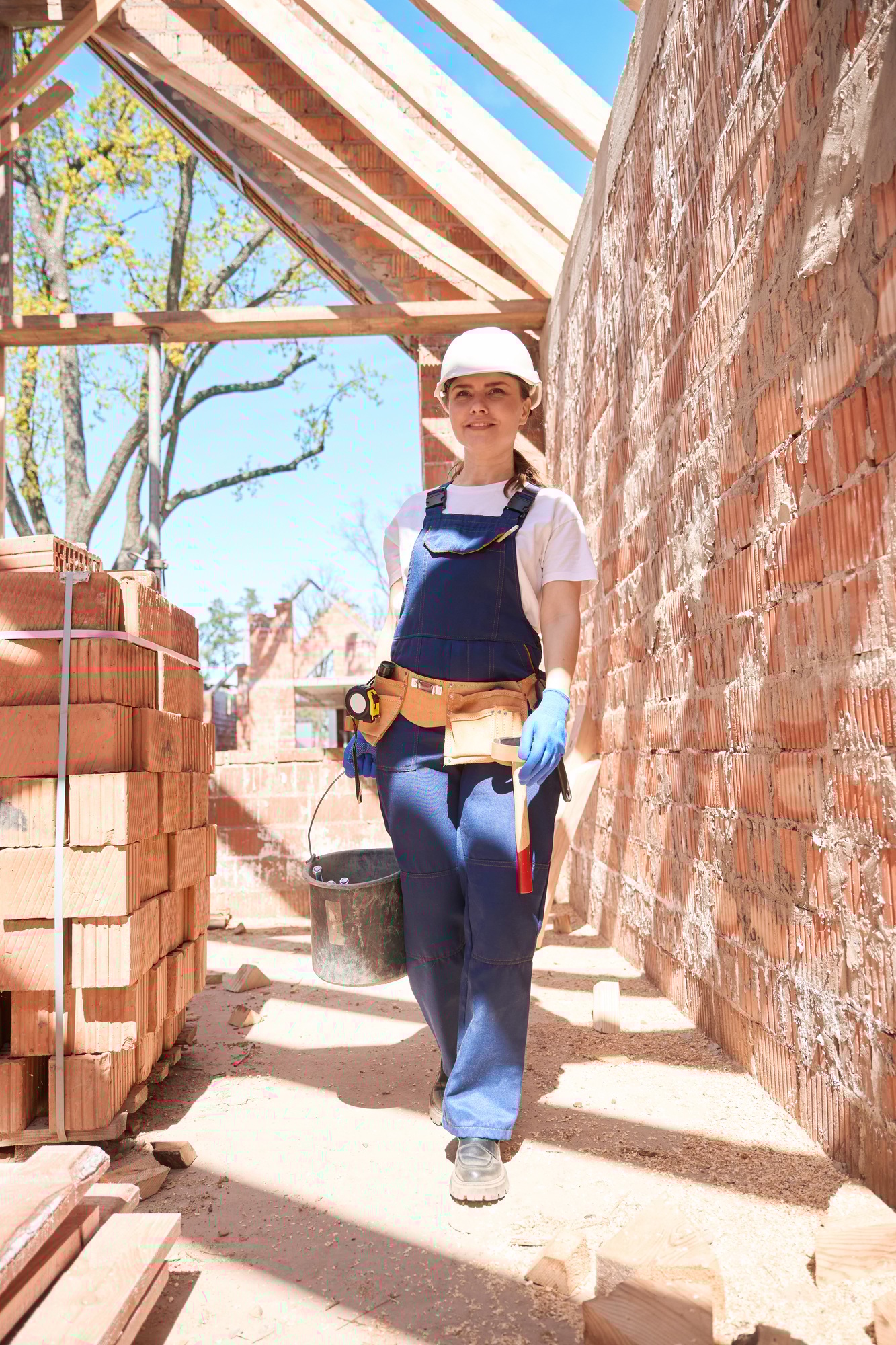 Woman builder carrying bucket with mortar, preparing material for bricklaying